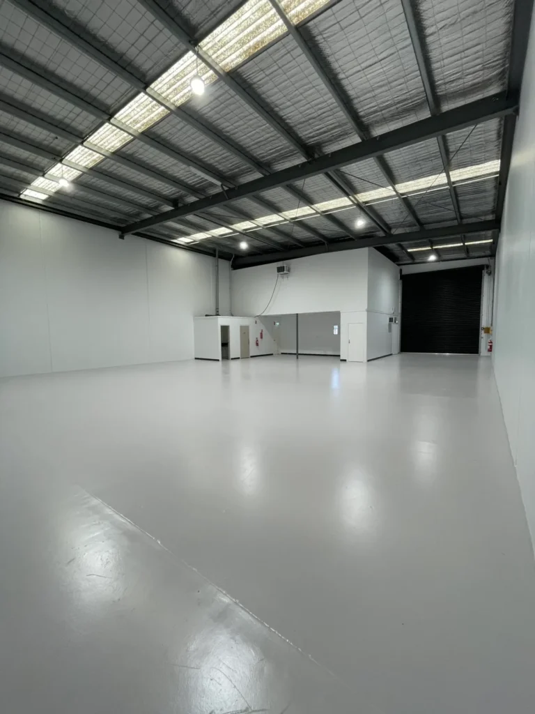 Large warehouse interior with freshly painted walls and sealed floor.