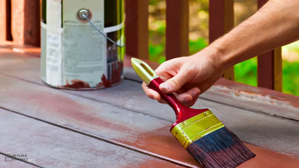 Hand staining a timber deck with a brush and wood stain.