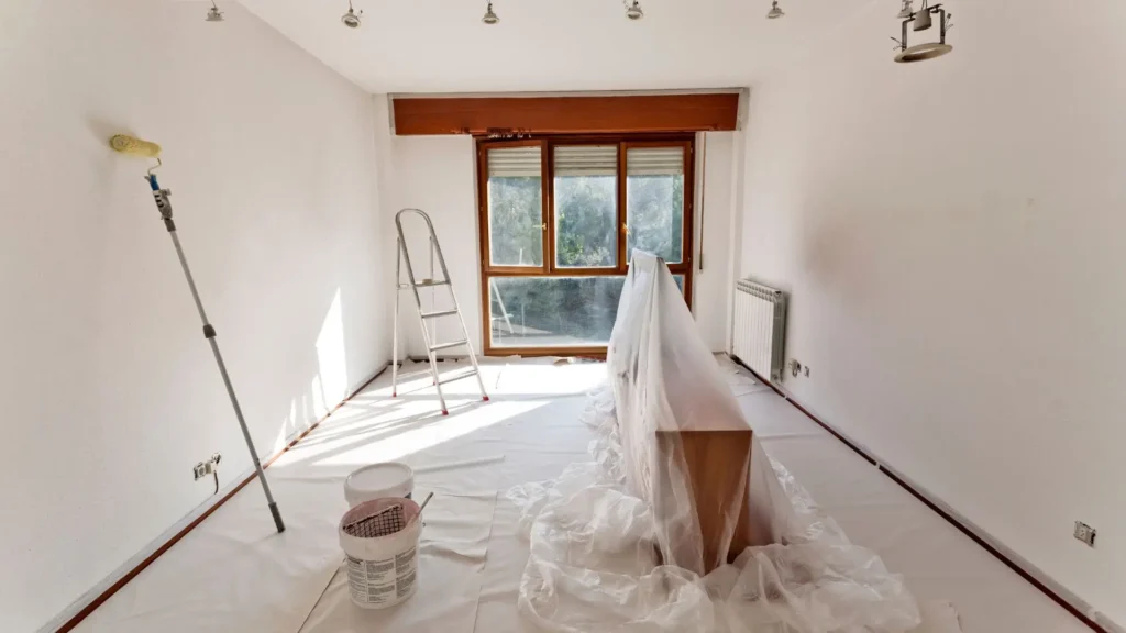 Office space prepared for painting with tools, drop sheets, and roller setup.